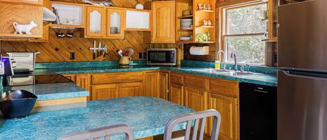 A kitchen with wooden cabinets, a granite countertop, a sink, a refrigerator, and a dining area with two chairs.