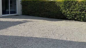 Een huis met een oprit van grind, een witte gevel en een rood dak.
