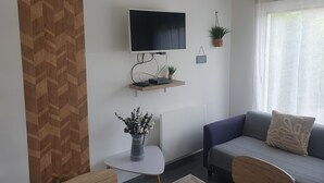Een woonkamer met een aan de muur bevestigde televisie, een bank, een salontafel en een bijzettafeltje met een plant.