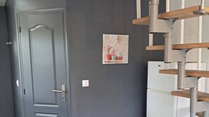 Een kamer met een grijze deur, een klein keukenhoekje met een koelkast en een houten stoel.