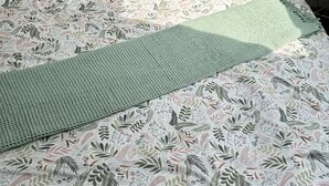 Een bed met een bloemenprint deken, twee roze kussens en een groene gebreide plaid.