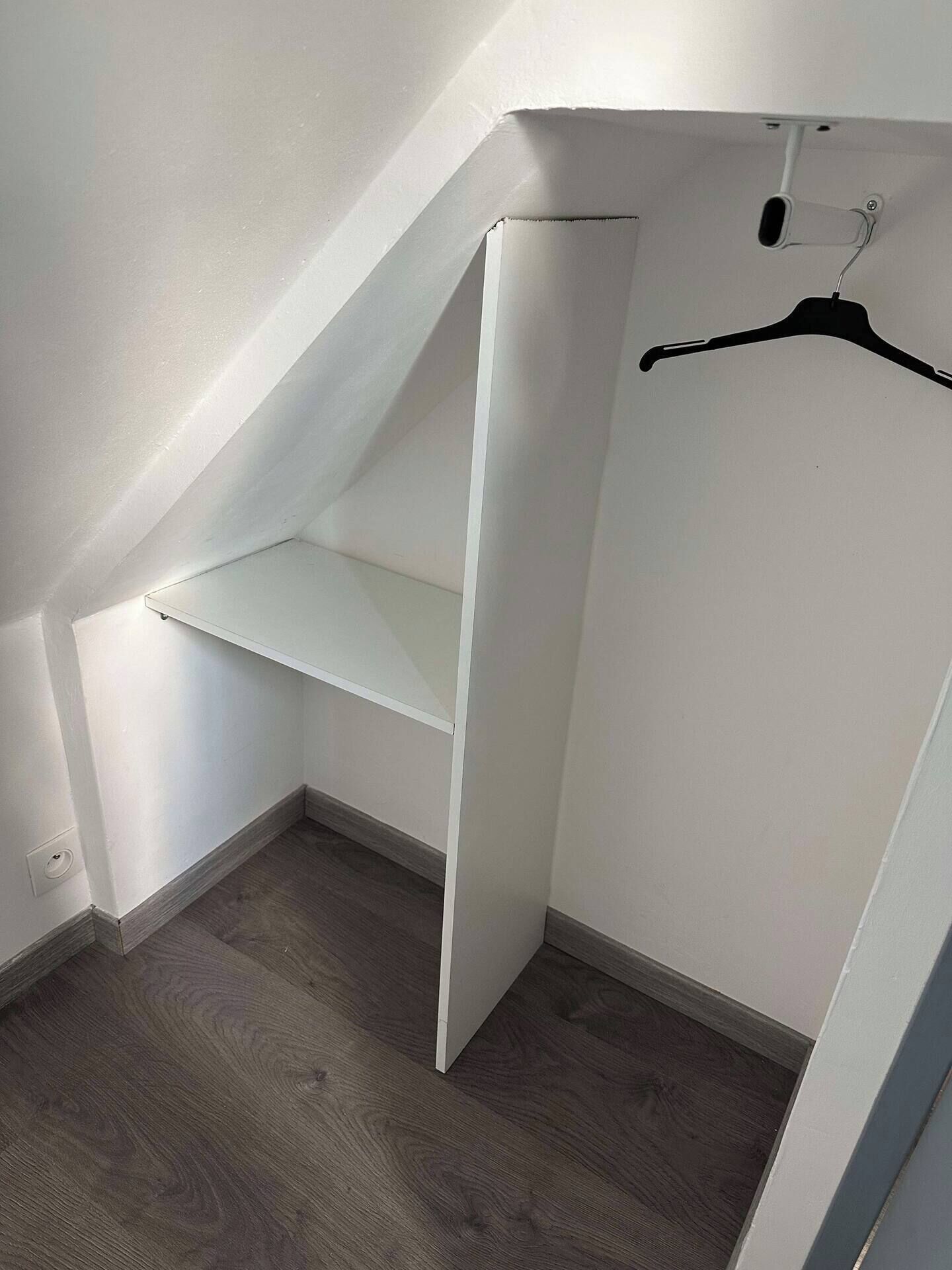 A small, enclosed closet space with a wooden floor and a white wall.