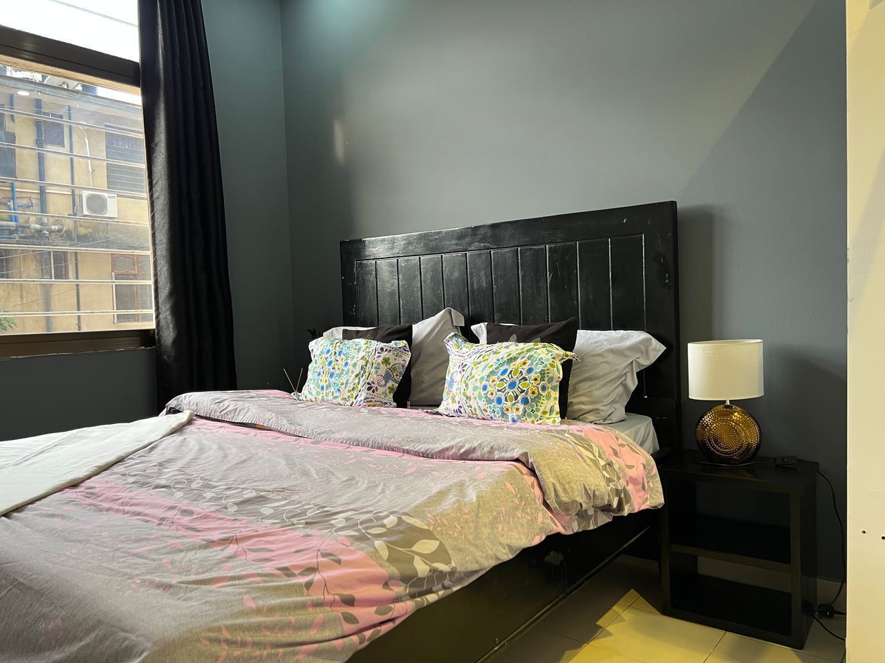 Un dormitorio con cama, almohadas, mesita de noche y lámpara.