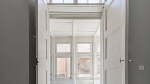 An open doorway leading to a room with a white desk, chair, and large windows. - Cozy Elegant 2BR Apartment (Valletta)