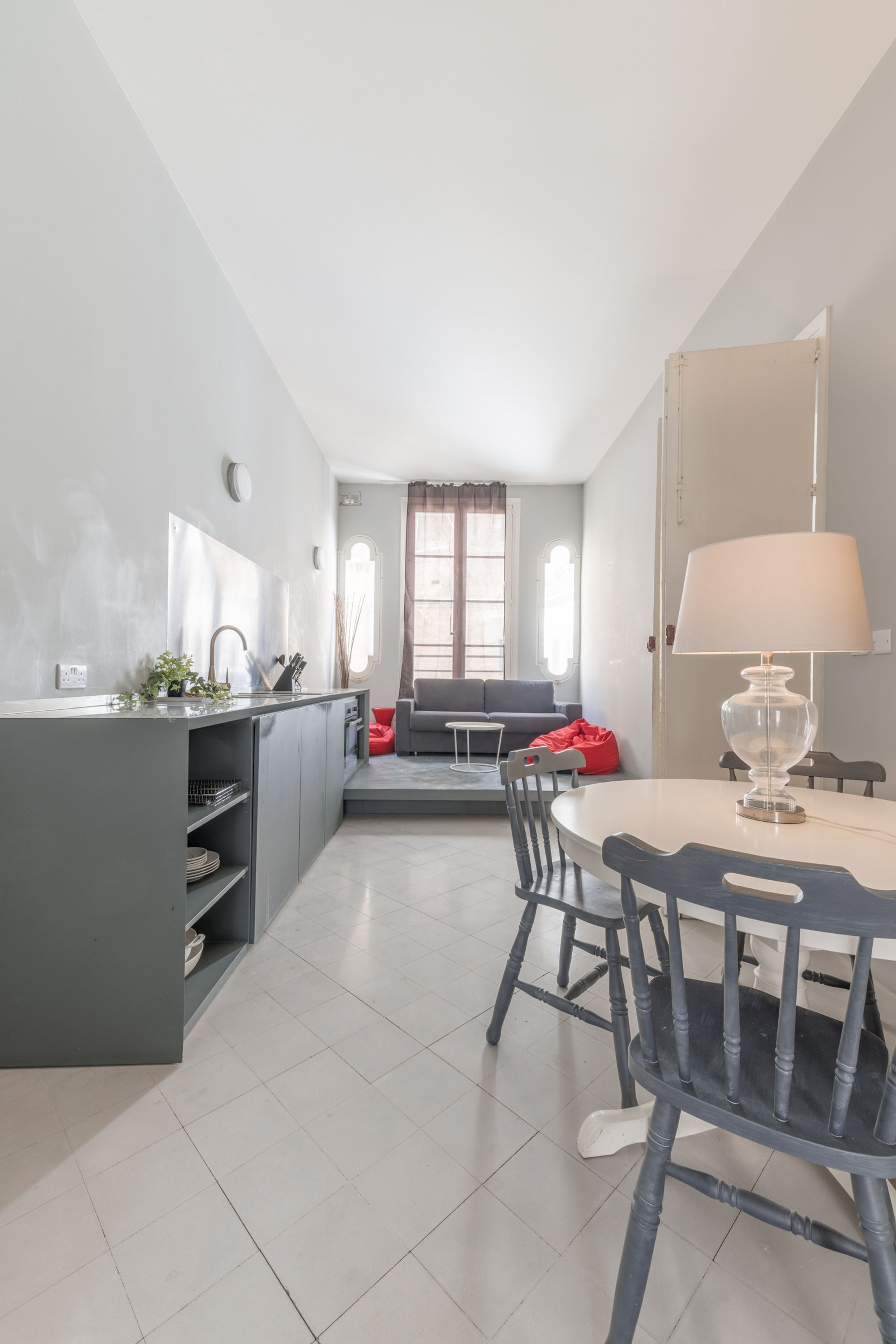 A compact kitchen with a dining area, a sofa, and a lamp.