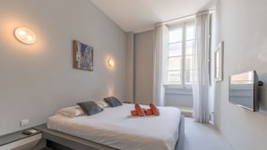 A modern bedroom with a bed, bedside table, artwork, and a TV. - Cozy Elegant 2BR Apartment (Valletta)