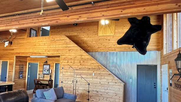 Un intérieur en bois avec un canapé, un tapis à carreaux et une tête d’animal fixée au mur.