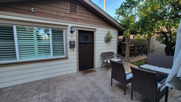 Una casa con un patio techado, mobiliario de mimbre y un pequeño jardín.