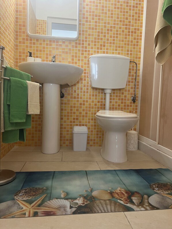 Un baño con lavamanos, inodoro y un revestimiento de azulejos. Hay toallas verdes colgadas en un perchero.