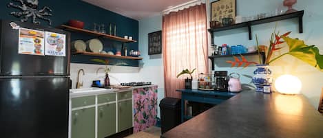 A kitchen with a black refrigerator, green cabinets, a pink floral backsplash, and a blue countertop.