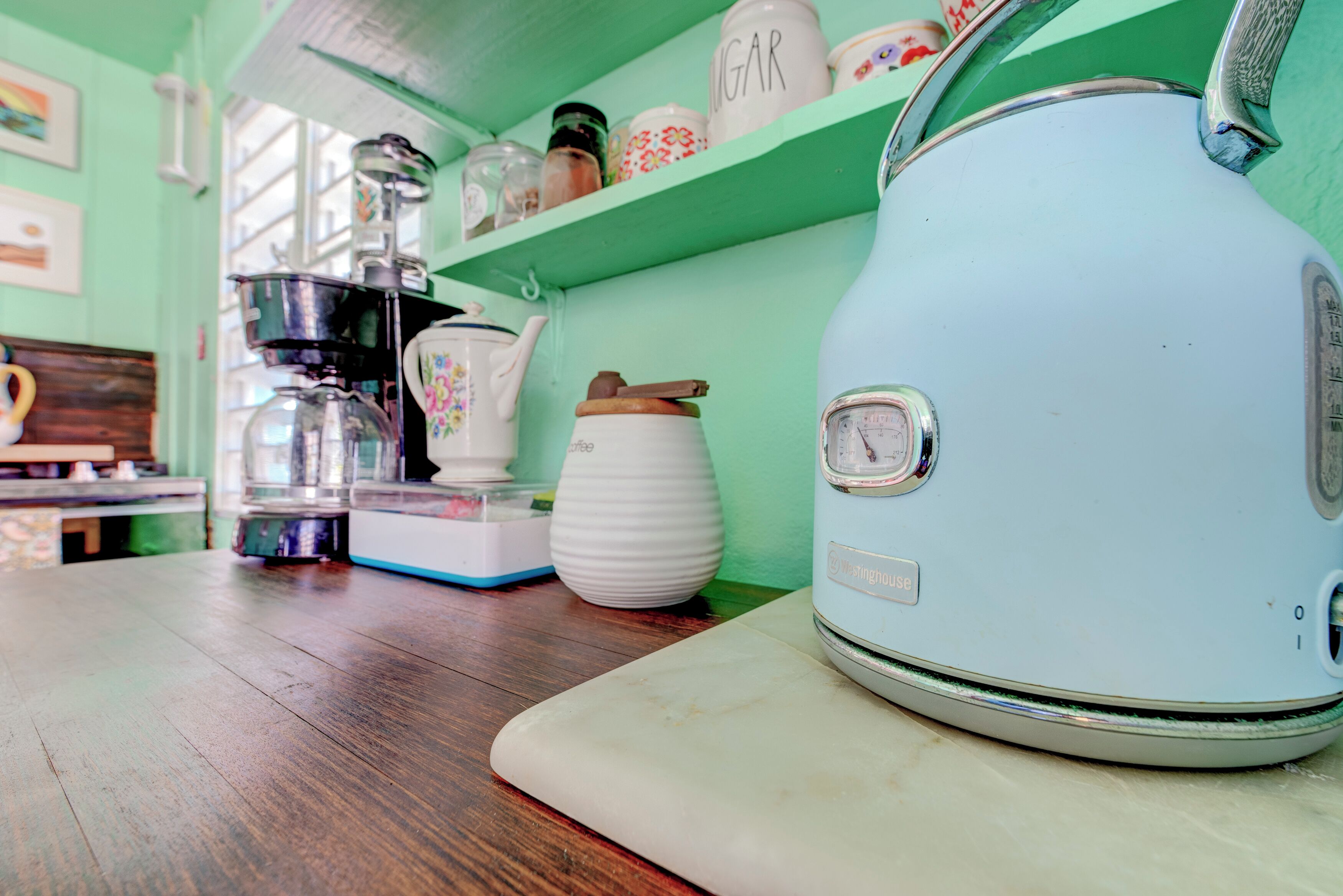 A kitchen with a light blue kettle, a coffee maker, and various jars on a green shelf.