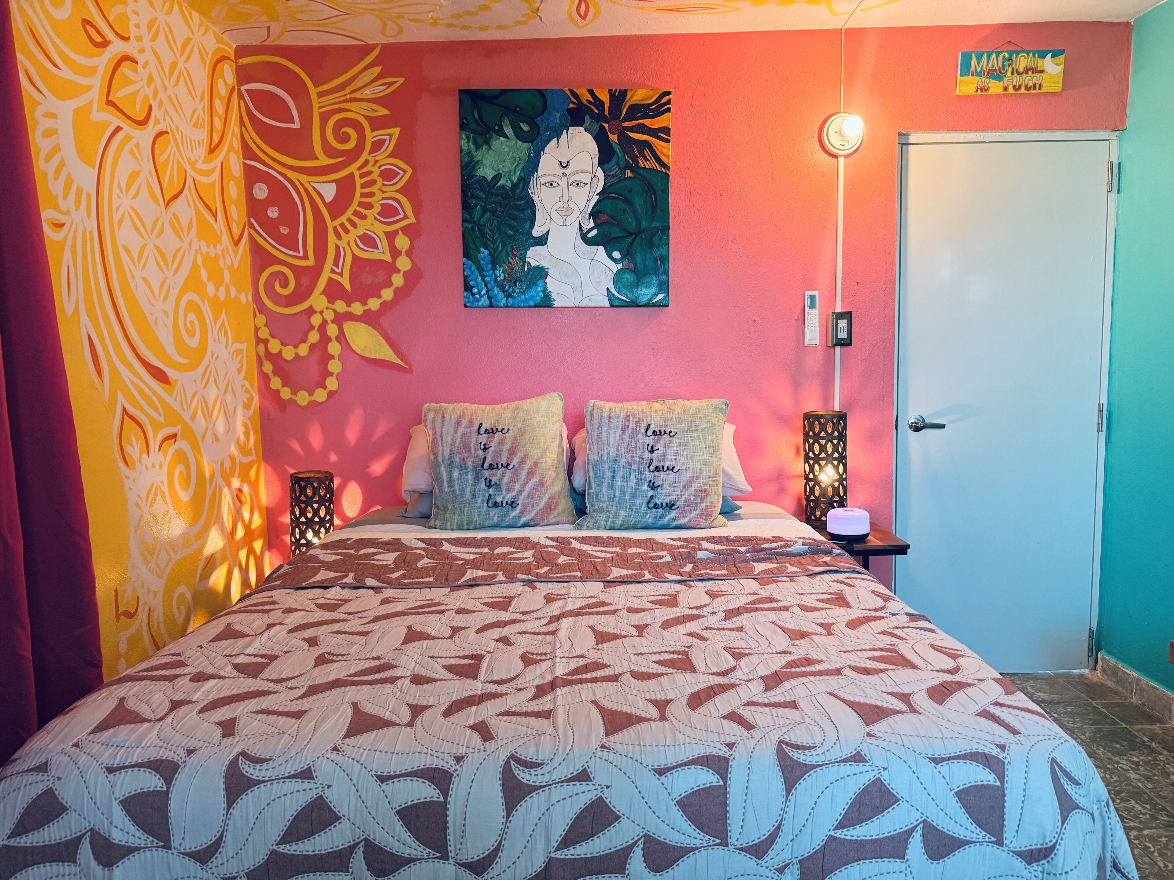 Una cama con ropa de cama estampada, una pared con un cuadro, una puerta y una mesita de noche con una lámpara.