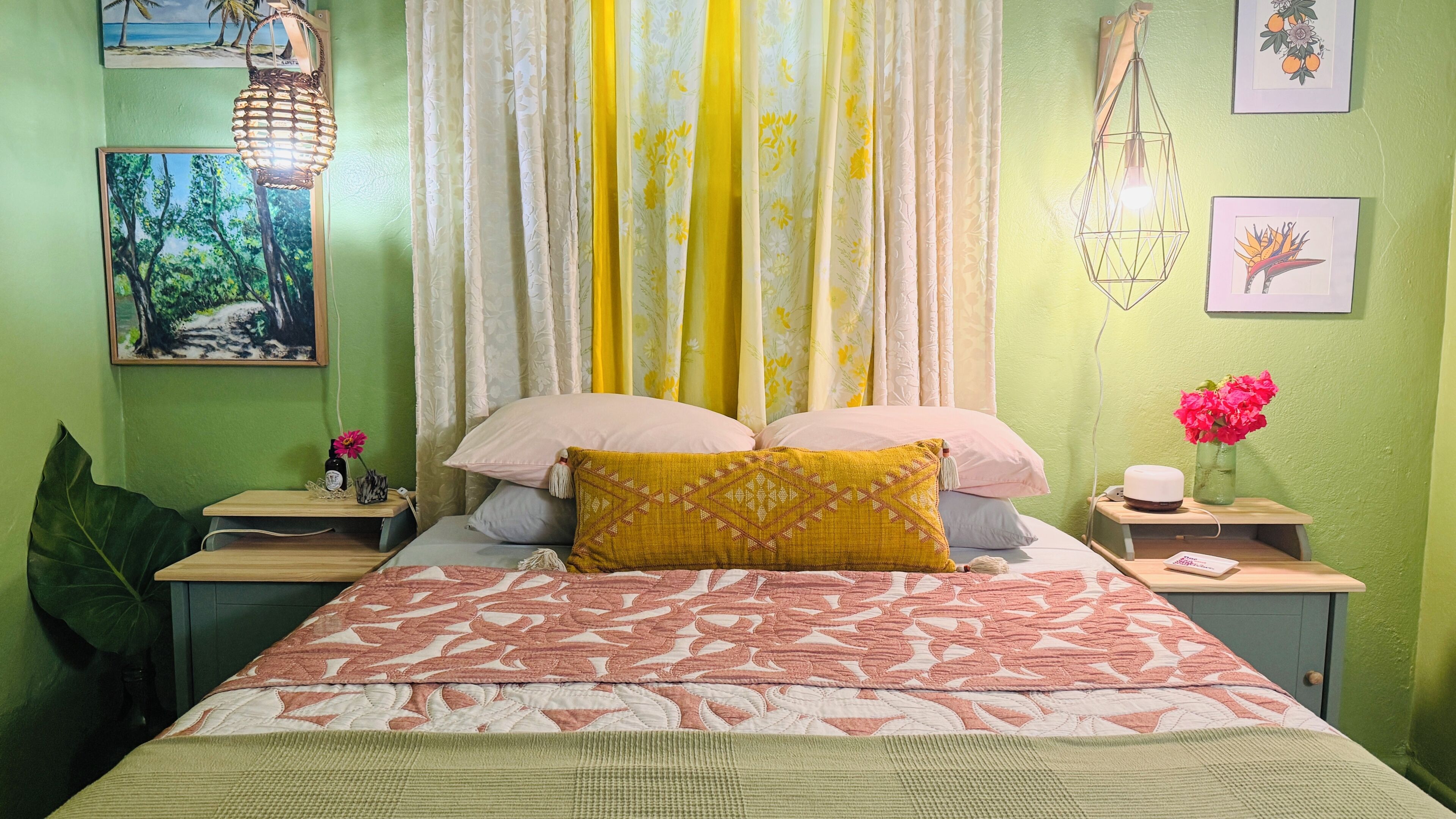 A room with a bed, green walls, a window with curtains, a bedside table with a lamp, and a wall-mounted light fixture.