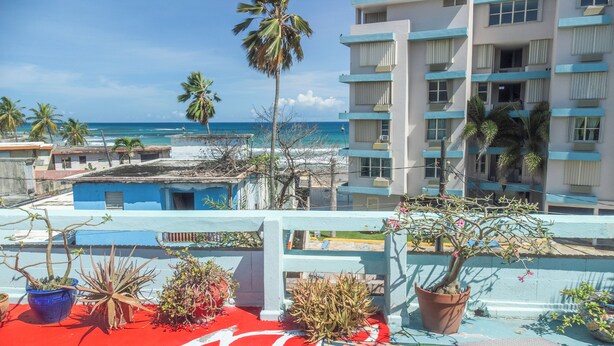 A hotel with a view of the ocean, featuring balconies with potted plants and a red carpet. - LoveSoulBeautiful (Luquillo)