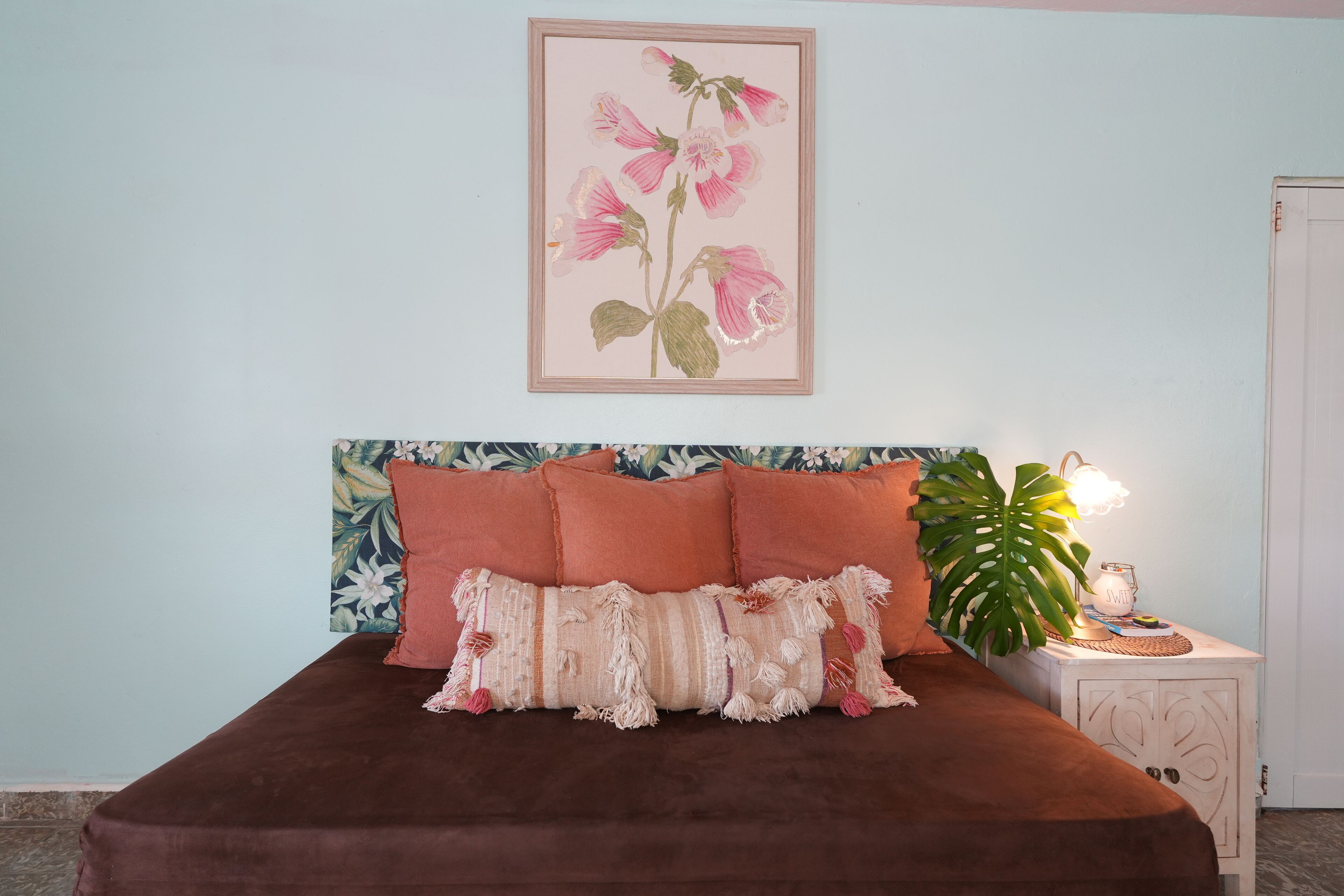 A bedroom with a bed, pillows, a nightstand, a lamp, and a wall-mounted picture.