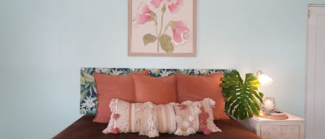 Un dormitorio con cama, almohadas, una mesita de noche, lámpara y un cuadro en la pared.