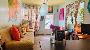 A cozy living room with a sofa, a television, a vase with flowers, and a chalkboard sign.