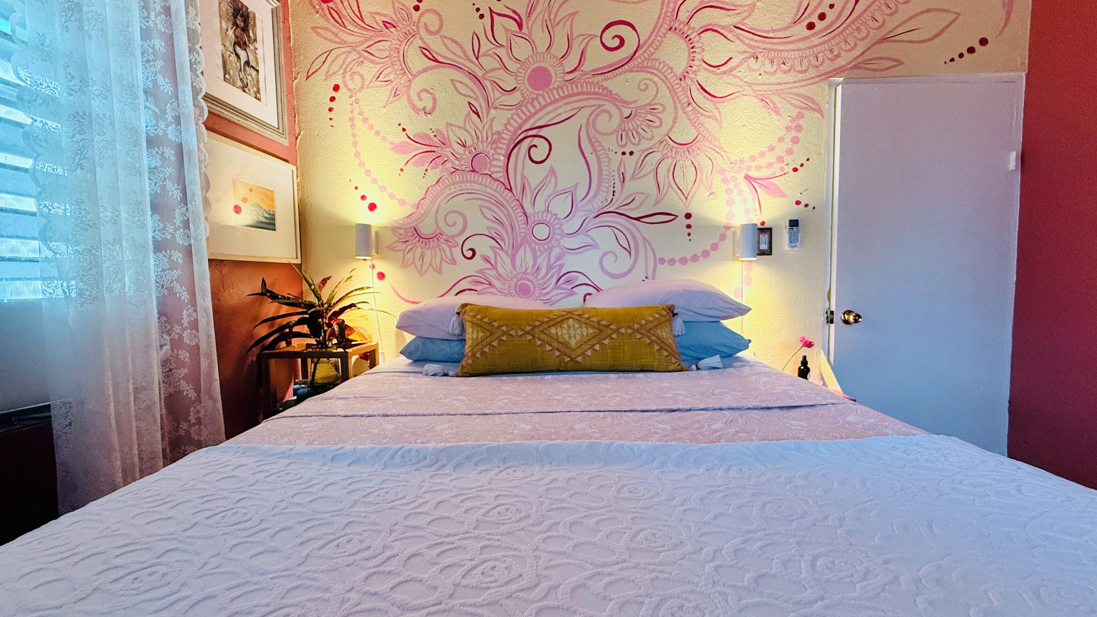 Ein Schlafzimmer mit einem Bett, einer blumengemusterten Wand, einer Tür und einem Fenster mit Vorhängen.