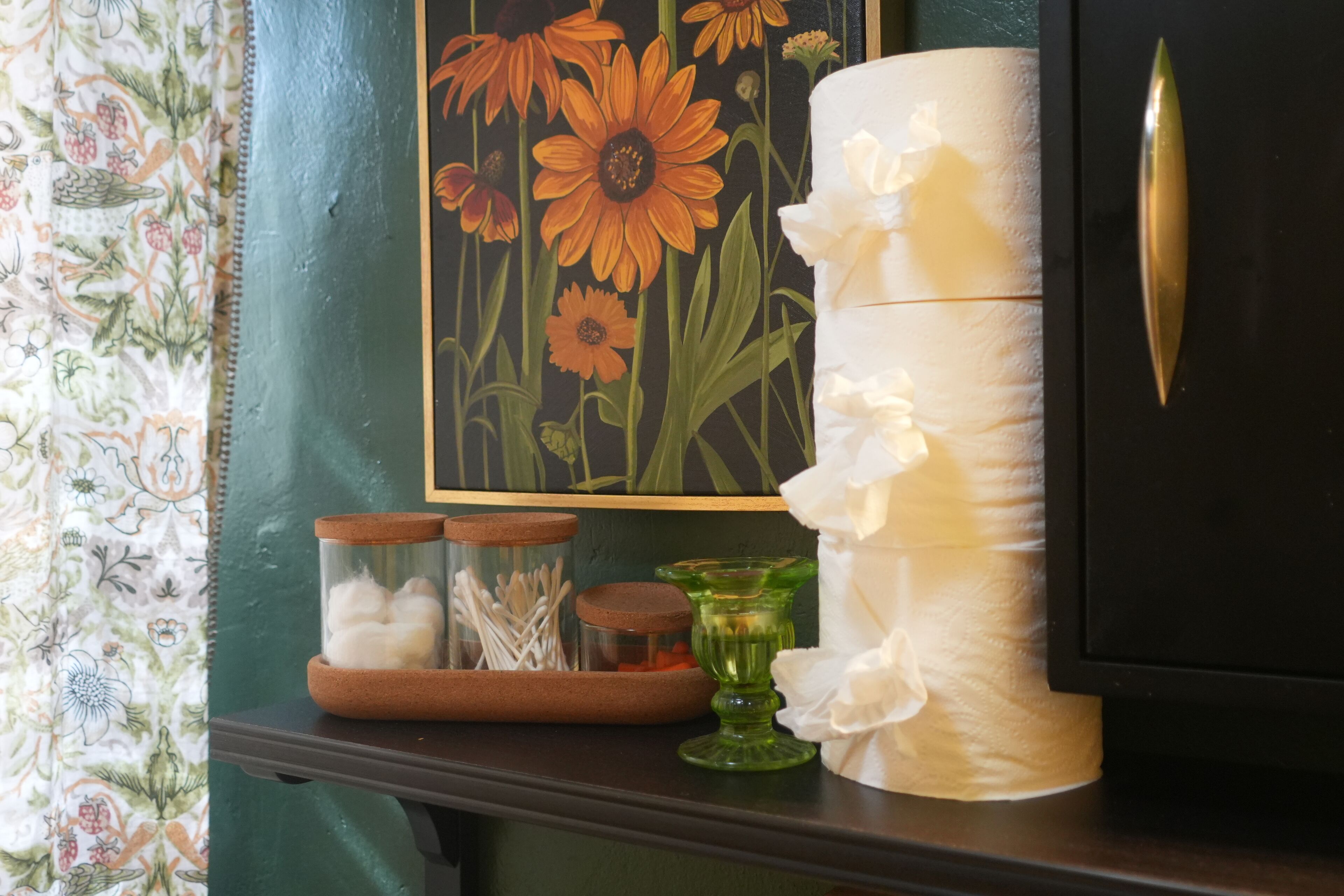 A shelf with a framed floral painting, a candle, and jars of cotton swabs.
