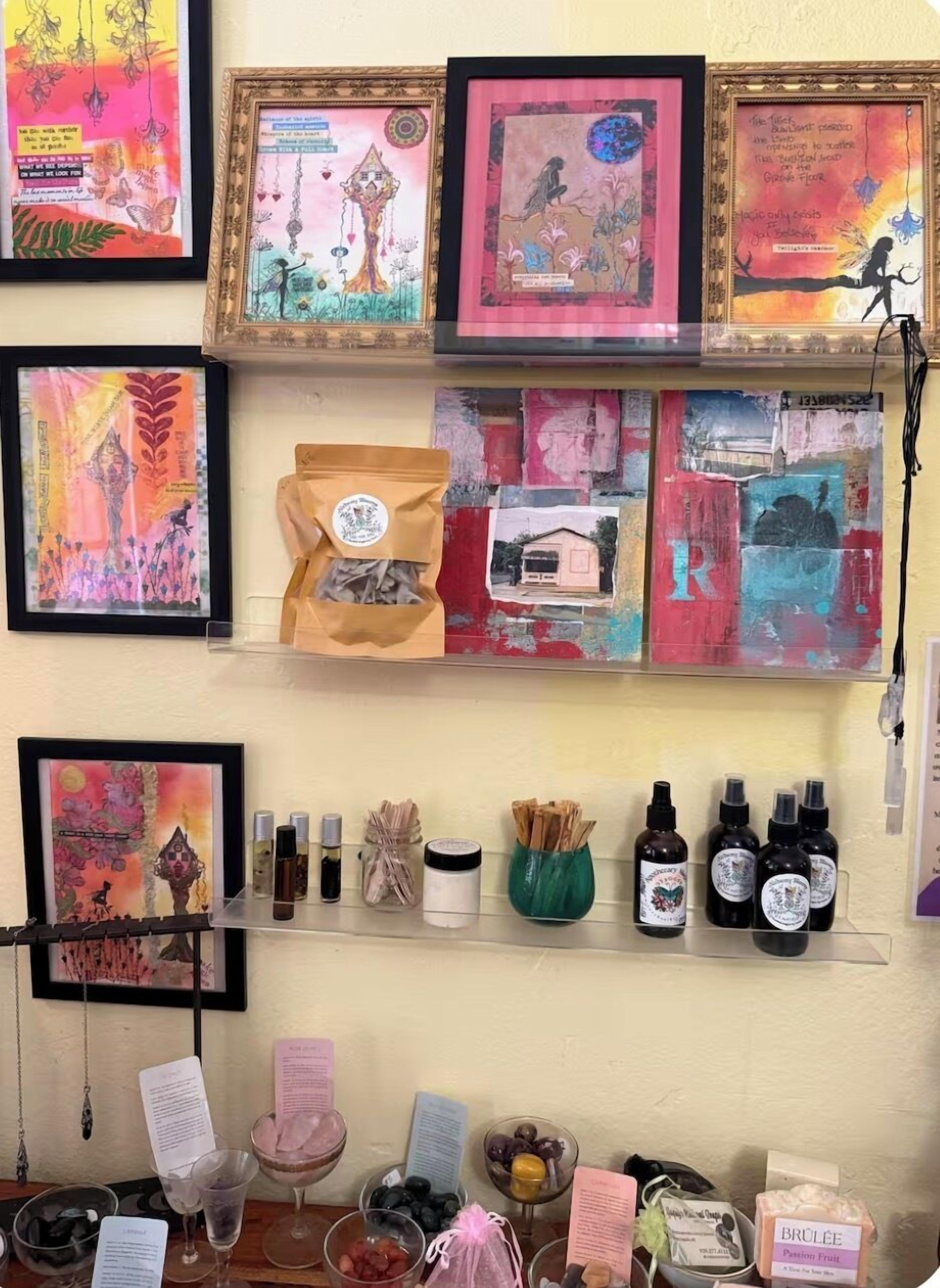 A wall with framed artwork, a shelf with bottles, and a table with various items.