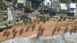 An aerial view of a beach with palm trees, a parking lot, and buildings. - LoveSoulBeautiful (Luquillo)