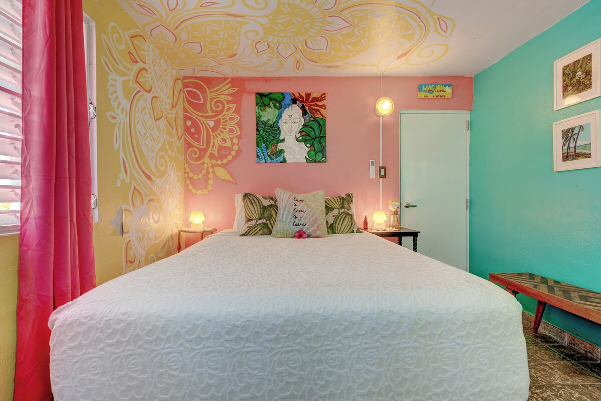 A bedroom with a bed, a wall mural, a door, and a bench.