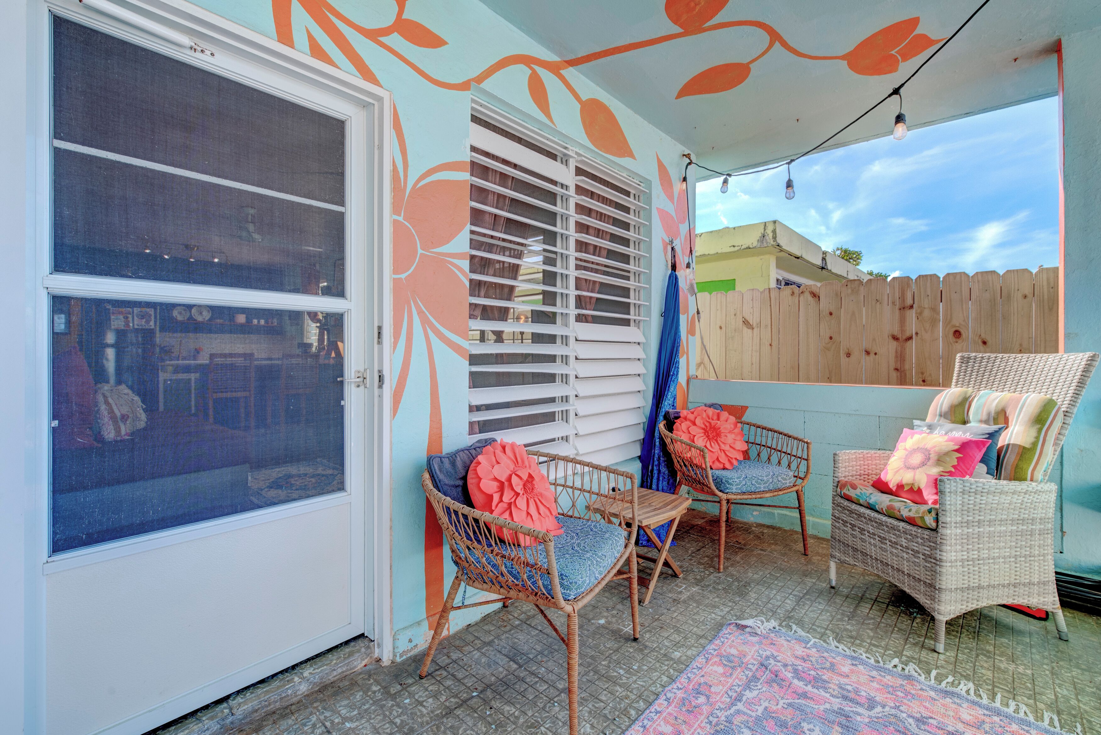 Un patio cubierto con sillas de mimbre, un tapiz estampado y una cerca de madera.
