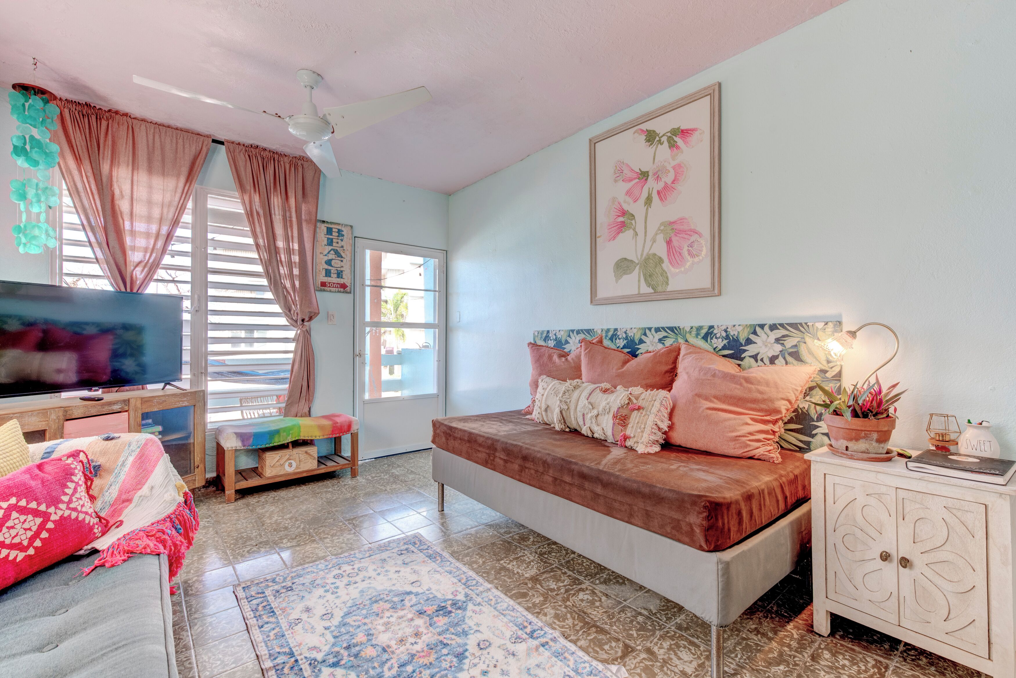 A bedroom with a bed, a TV, a desk, and a window with curtains.
