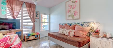 A bedroom with a bed, a TV, a desk, and a window with curtains.