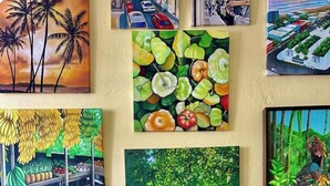A wall with various paintings, a wooden table with jewelry, and a large green leaf. - LoveSoulBeautiful (Luquillo)