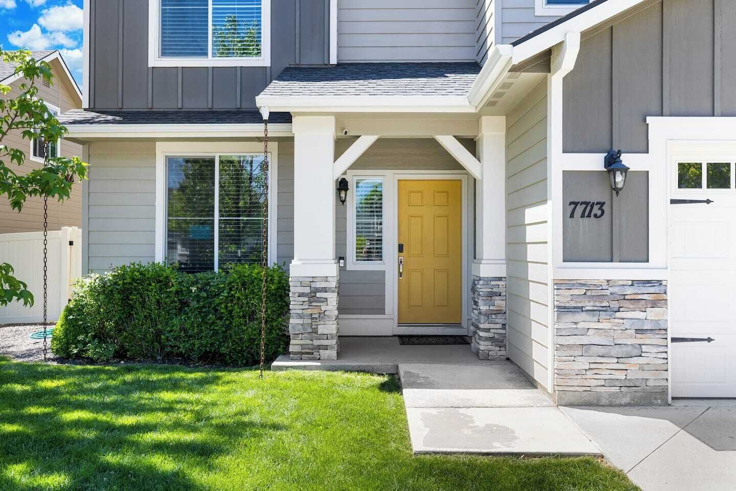 A two-story house with a stone foundation, a yellow front door, and a mailbox with the number 7713.