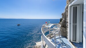 A balcony with a view of the sea, a small boat, and a table with drinks.