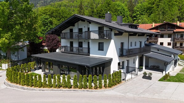 Un bâtiment moderne à deux étages, doté de balcons, d’un patio couvert et d’un jardin aménagé.