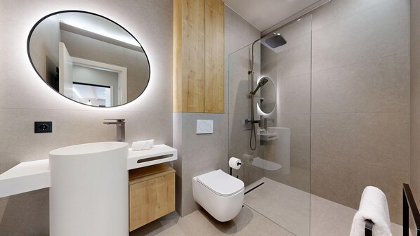 Une salle de bain moderne avec un grand miroir rond, un lavabo sur pied, des toilettes et une douche à parois de verre.