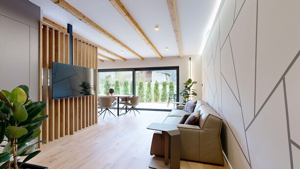 A modern living room with a wooden ceiling, a flat-screen TV, a sofa, and a dining area with a table and chairs. - Stay Here Living  (Thiersee)