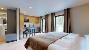 A modern hotel room with a large bed, a separate kitchenette, a sitting area, and a balcony with curtains. - Stay Here Living  (Thiersee)