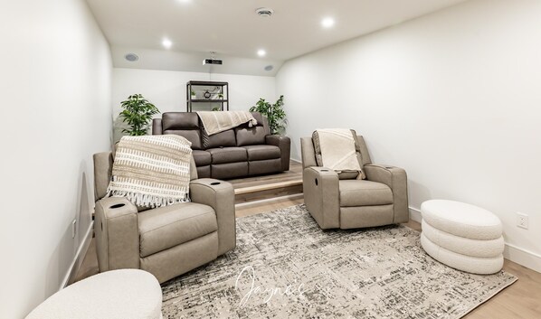 Un salon moderne avec un canapé en cuir marron, deux fauteuils, un pouf blanc et un tapis à motifs.