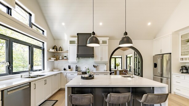 Une cuisine moderne dotée d’un grand îlot central, de luminaires suspendus et offrant une vue sur l’extérieur grâce à de grandes fenêtres.