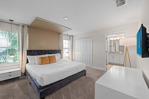 A bedroom with a large bed, a bedside table, a desk, a wardrobe, and a bathroom with a mirror and sink.