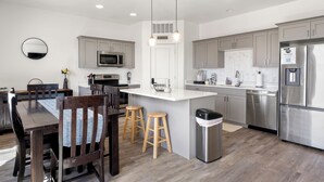 Een moderne keuken met een centraal eiland, houten stoelen en roestvrijstalen apparatuur.