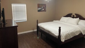 Een slaapkamer met een bed, een plafondventilator, een raam met jaloezieën en een schilderij aan de muur.