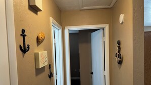 Een smalle gang met beige muren, een witte deur en een kleine houten deur. Twee zwarte wandankers en een klein houten object zijn op de muur te zien.