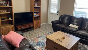Een woonkamer met een televisie, houten planken, een leren bank en een salontafel.