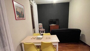 Un coin repas avec une table et quatre chaises jaunes, un canapé noir et un téléviseur posé sur un meuble.