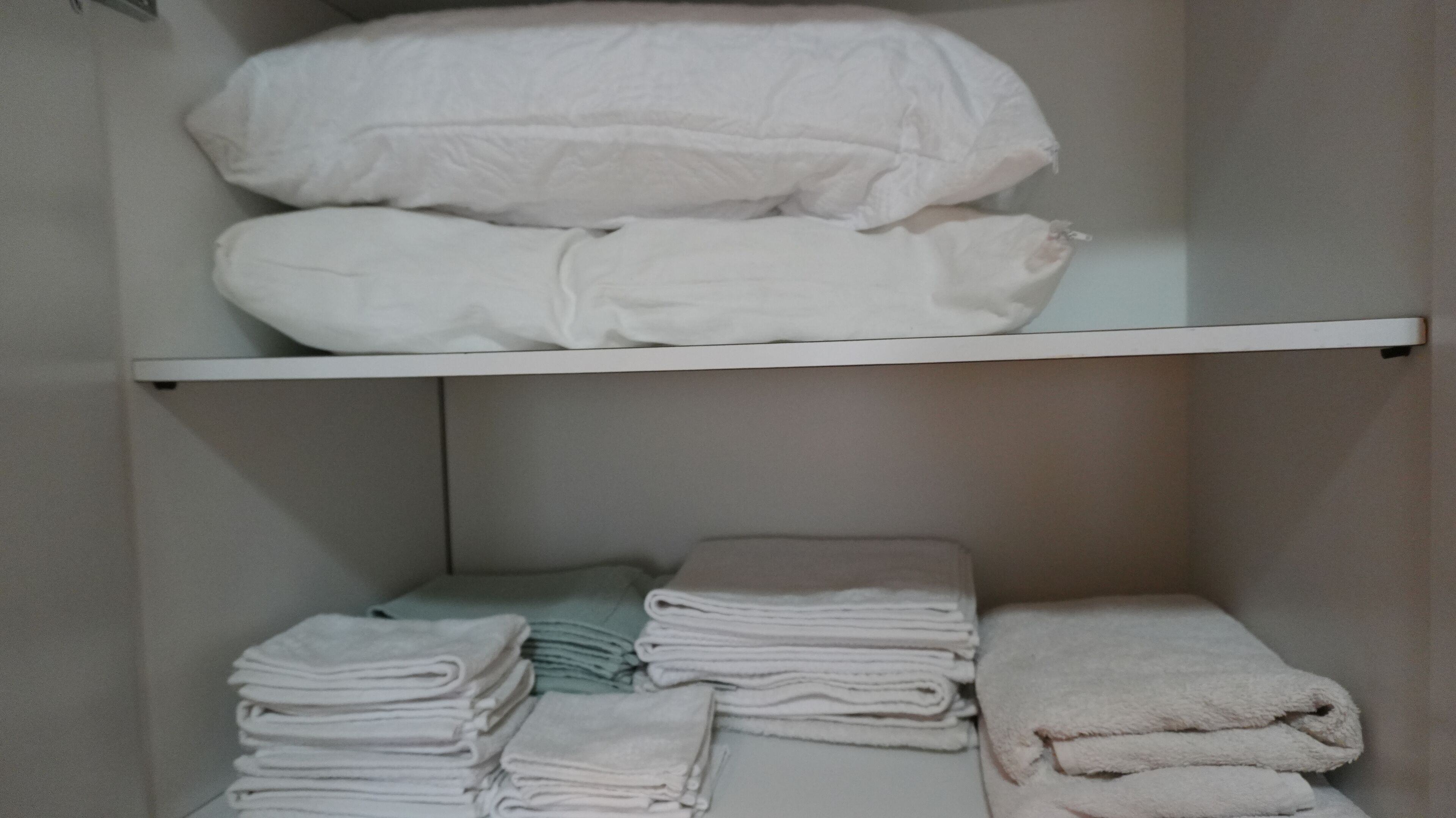 Un'area di stoccaggio con asciugamani bianchi ordinatamente impilati e coperte piegate sugli scaffali.