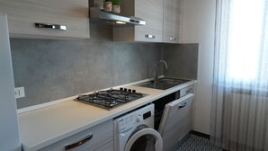 Une cuisine compacte équipée d’une cuisinière à gaz, d’un évier et d’un lave-linge encastré.