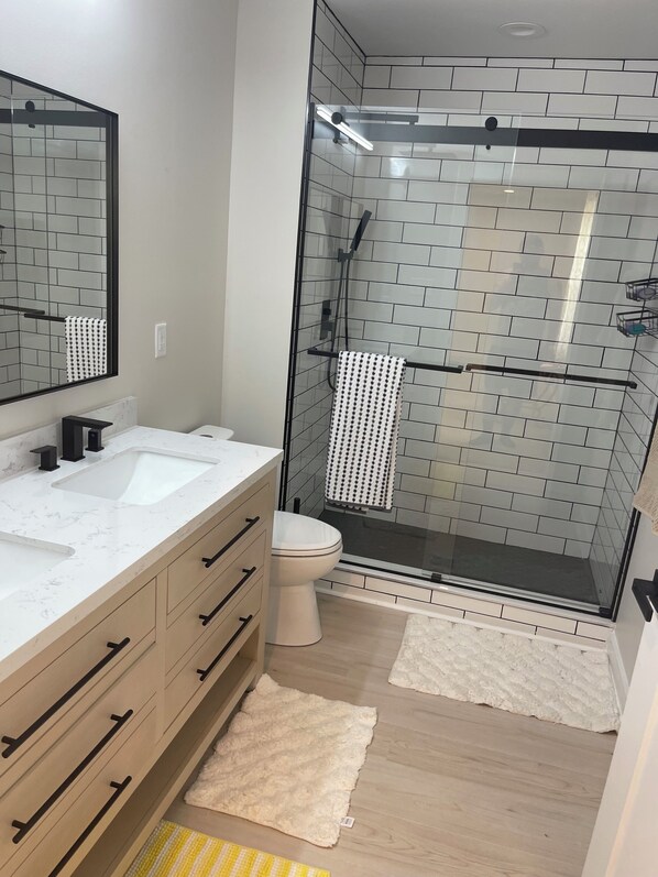 A modern bathroom with two sinks, a toilet, and a glass-enclosed shower.