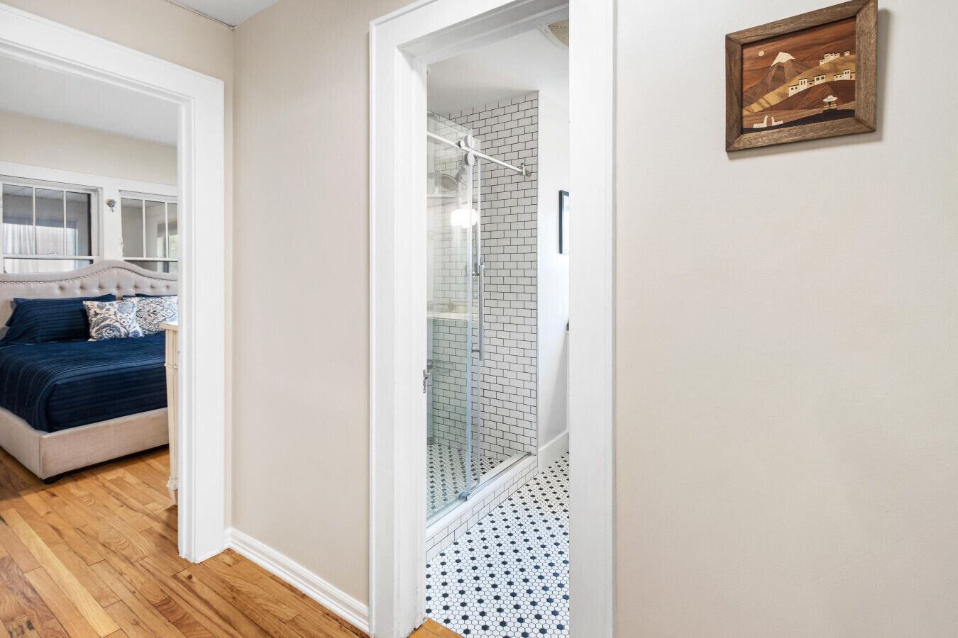 Une chambre avec un lit, une salle de bain avec une douche et un couloir orné d’un tableau encadré.