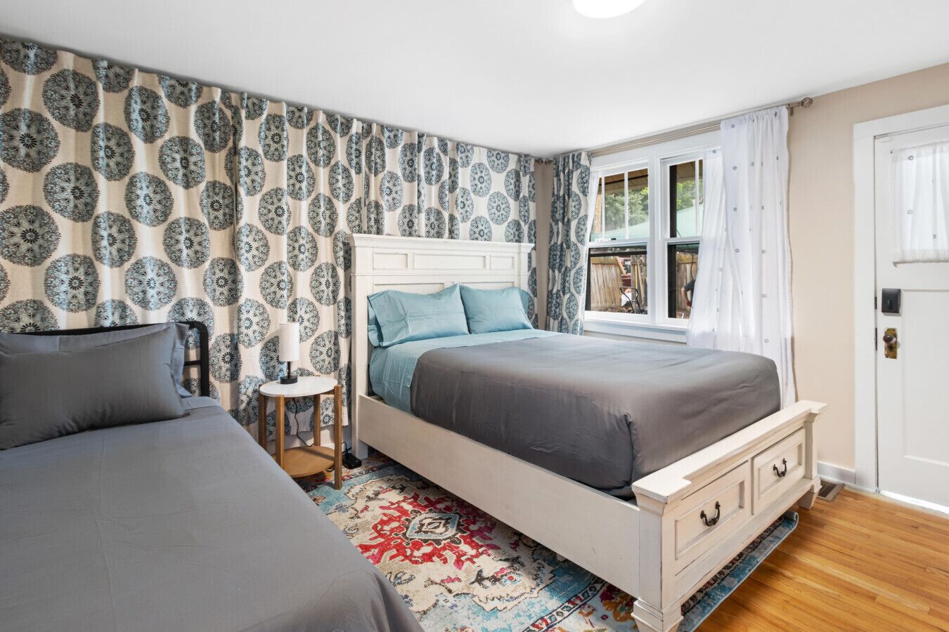 Ein Schlafzimmer mit zwei Betten, einem Fenster mit Vorhängen, einer Wand mit Muster und einem kleinen Tisch.