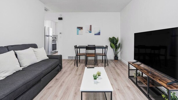 A modern living room with a sofa, dining table, chairs, a TV, and a kitchen area. - Cozy Salt Lake Getaway - Desk w/ Monitor ! (Salt Lake City)